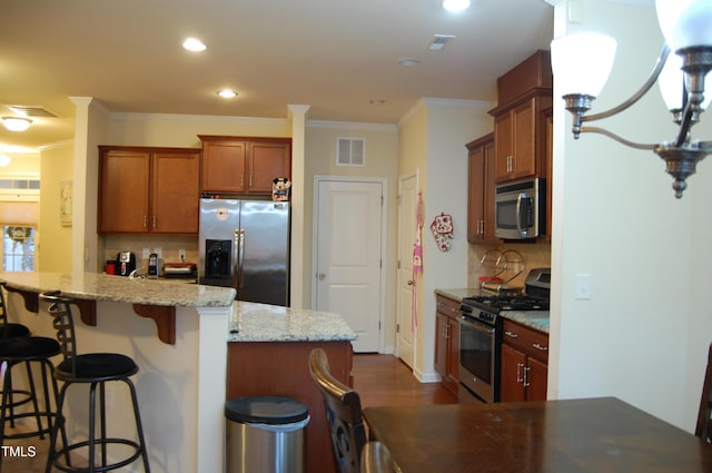 kitchen featuring light stone countertops, ornamental molding, appliances with stainless steel finishes, tasteful backsplash, and a kitchen bar