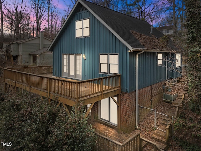 back house at dusk featuring a wooden deck and cooling unit