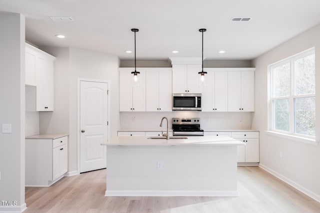 kitchen featuring light wood-type flooring, stainless steel appliances, sink, hanging light fixtures, and an island with sink