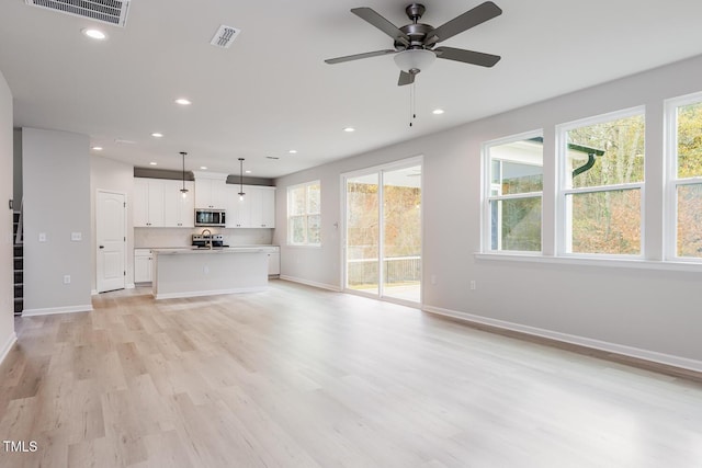 unfurnished living room with sink, light wood-type flooring, plenty of natural light, and ceiling fan