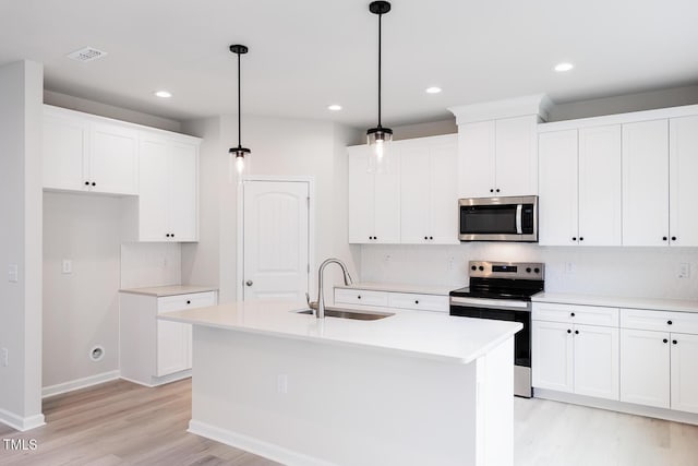 kitchen featuring sink, an island with sink, light hardwood / wood-style floors, decorative light fixtures, and appliances with stainless steel finishes