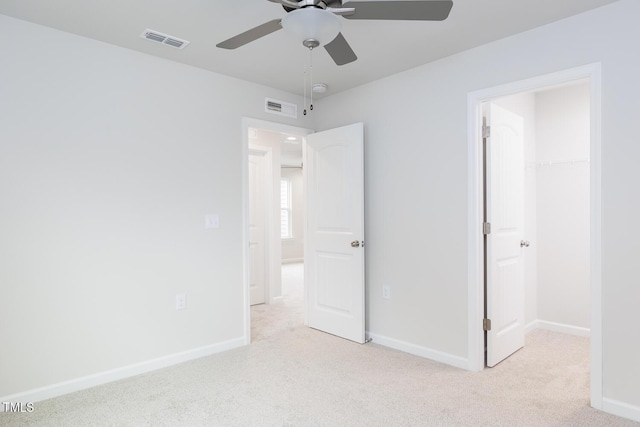 unfurnished bedroom featuring a walk in closet, ceiling fan, a closet, and light carpet