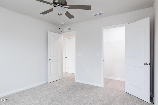 unfurnished bedroom with a walk in closet, ceiling fan, a closet, and light carpet