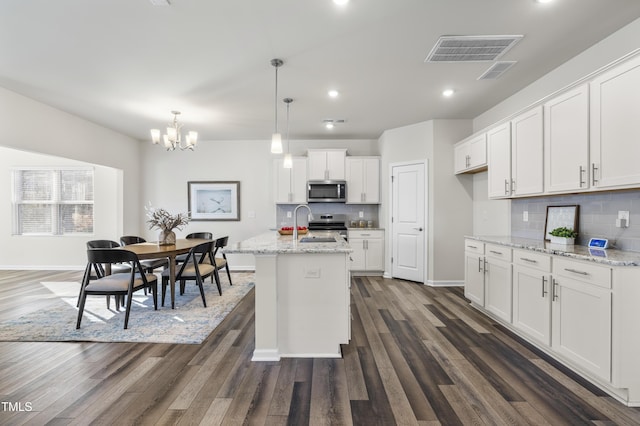 kitchen featuring white cabinetry, appliances with stainless steel finishes, a kitchen island with sink, light stone countertops, and pendant lighting