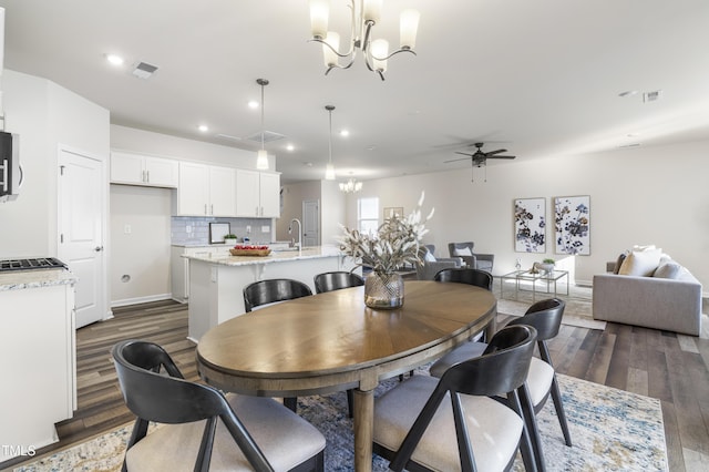 dining space featuring ceiling fan with notable chandelier, dark wood-type flooring, and sink