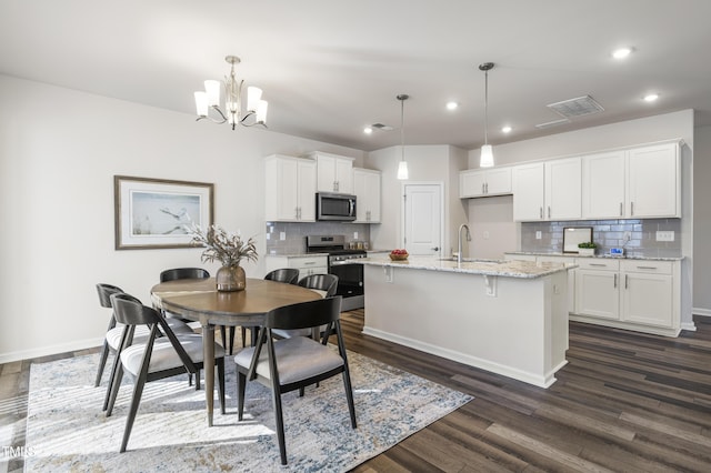 kitchen featuring decorative light fixtures, white cabinetry, appliances with stainless steel finishes, and a kitchen island with sink