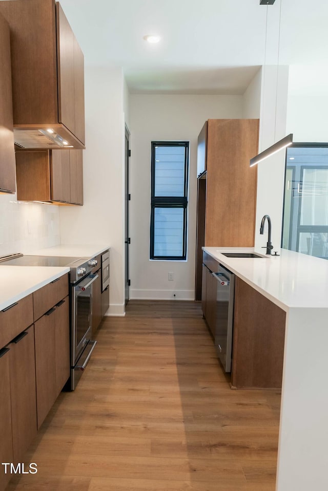 kitchen with kitchen peninsula, light wood-type flooring, stainless steel appliances, sink, and pendant lighting