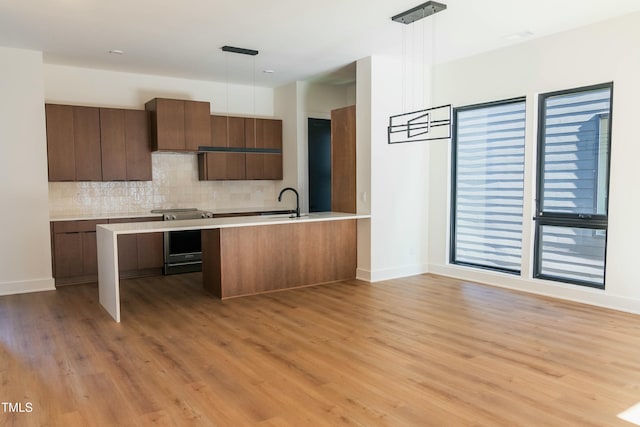 kitchen featuring electric range, light hardwood / wood-style floors, hanging light fixtures, and tasteful backsplash