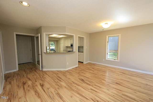 unfurnished living room featuring plenty of natural light, light hardwood / wood-style floors, and a textured ceiling