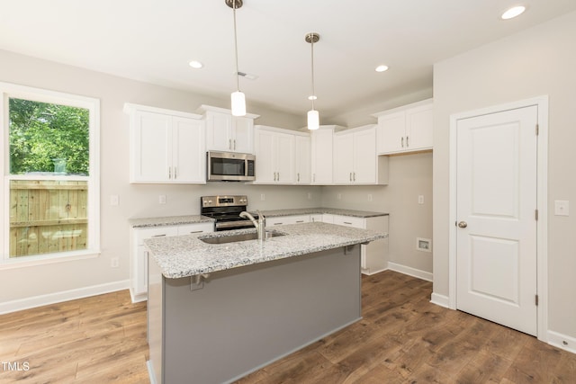 kitchen featuring light stone countertops, stainless steel appliances, a center island with sink, hardwood / wood-style flooring, and white cabinets