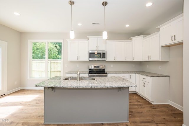 kitchen featuring light stone countertops, appliances with stainless steel finishes, a kitchen island with sink, white cabinets, and hanging light fixtures