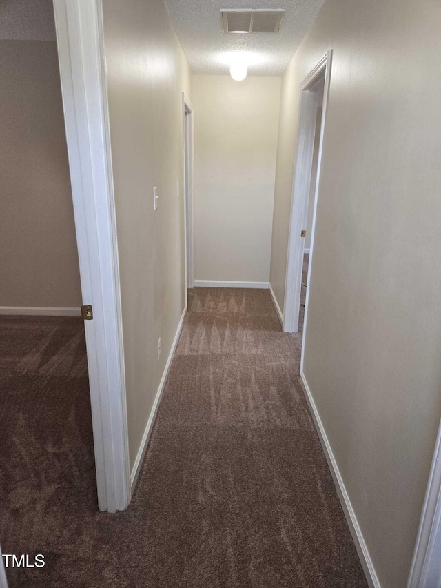 hall with dark colored carpet and a textured ceiling