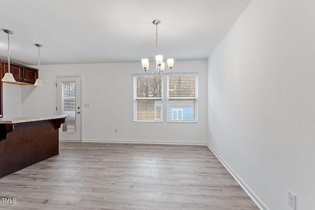 unfurnished dining area with a notable chandelier, a healthy amount of sunlight, and light hardwood / wood-style flooring