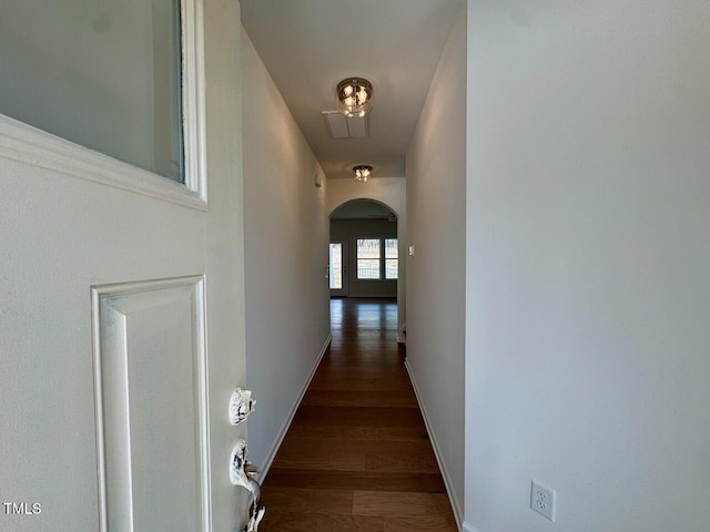 corridor with arched walkways, wood finished floors, and baseboards