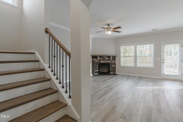 unfurnished living room featuring ceiling fan, ornamental molding, a fireplace, and light wood-type flooring