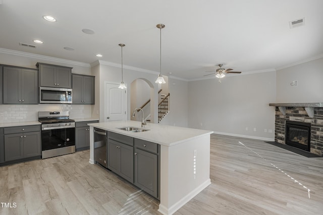 kitchen with gray cabinetry, sink, stainless steel appliances, and a center island with sink