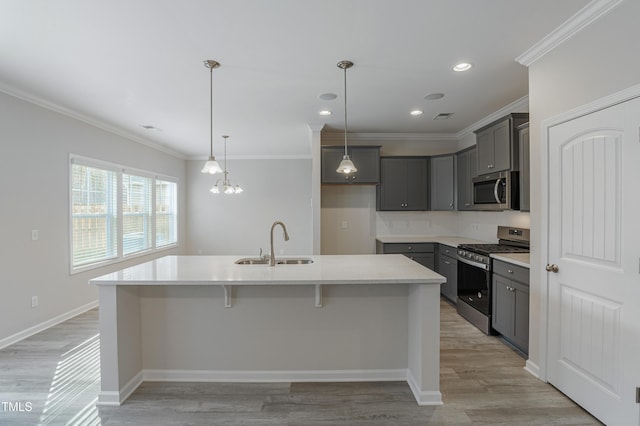 kitchen featuring sink, hanging light fixtures, stainless steel appliances, a center island with sink, and light wood-type flooring