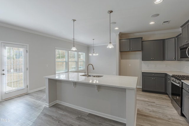 kitchen with sink, a kitchen island with sink, hanging light fixtures, stainless steel appliances, and ornamental molding