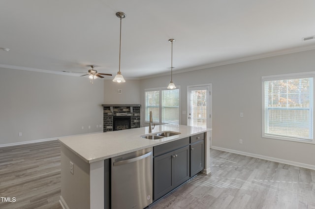 kitchen featuring a stone fireplace, sink, decorative light fixtures, stainless steel dishwasher, and an island with sink