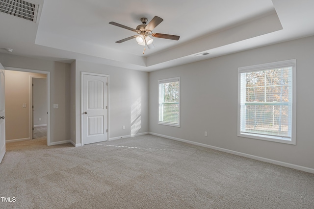 spare room featuring ceiling fan, light colored carpet, and a tray ceiling