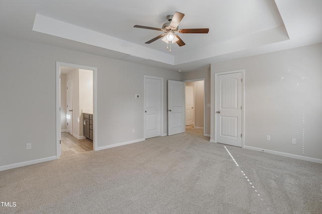 unfurnished bedroom with a tray ceiling, ensuite bath, and light colored carpet