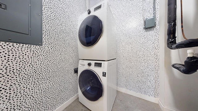 clothes washing area featuring laundry area, stacked washing maching and dryer, and baseboards