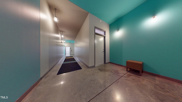 corridor featuring lofted ceiling, finished concrete floors, and baseboards