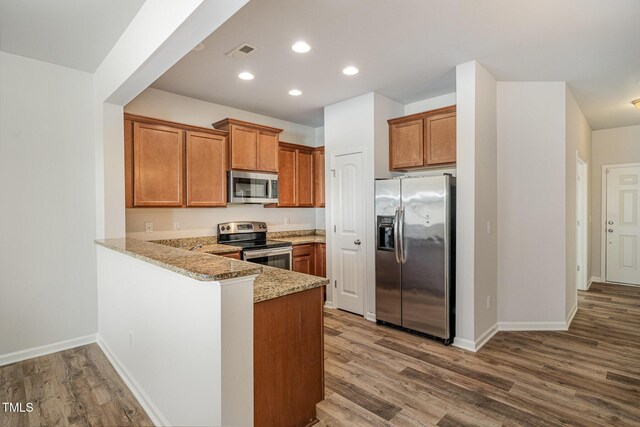 kitchen with kitchen peninsula, hardwood / wood-style floors, stainless steel appliances, and light stone counters