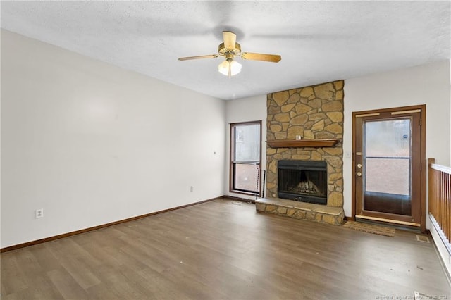 unfurnished living room with a textured ceiling, dark hardwood / wood-style floors, a stone fireplace, and ceiling fan