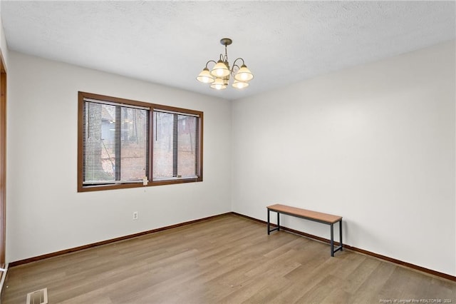 empty room with a notable chandelier, light wood-type flooring, and a textured ceiling