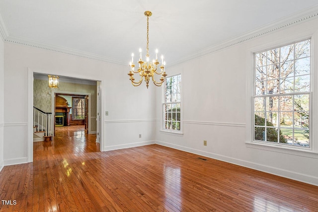 unfurnished dining area featuring wood-type flooring, crown molding, and a notable chandelier