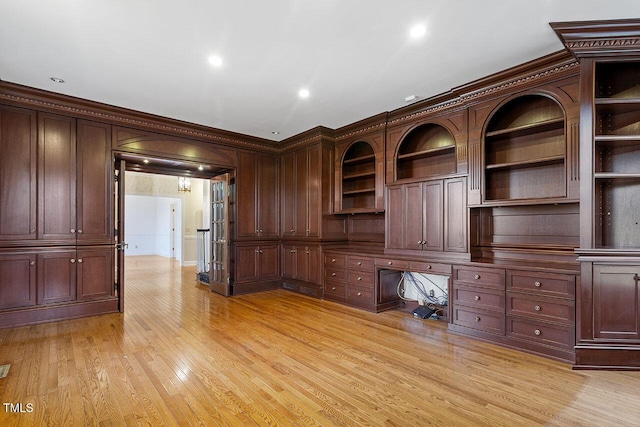 unfurnished office with built in desk, crown molding, and light hardwood / wood-style flooring