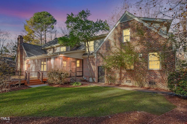 back house at dusk with a lawn, a wooden deck, and a sunroom