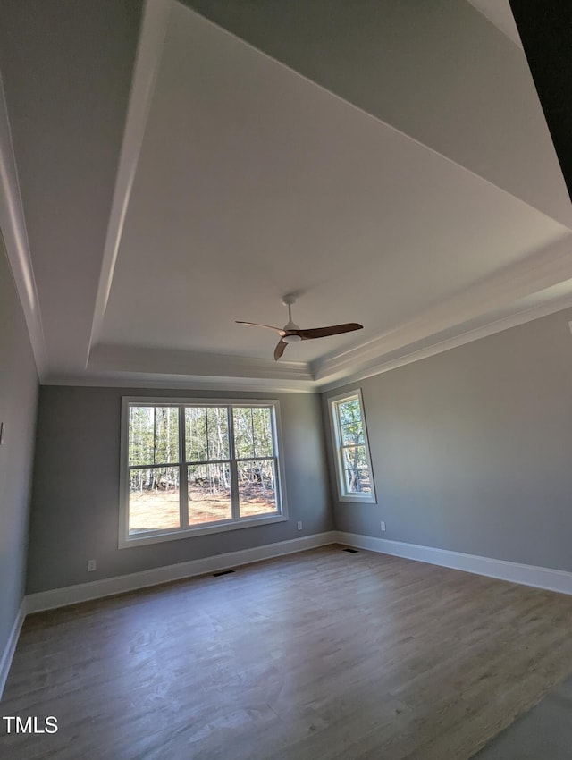 empty room with ceiling fan, ornamental molding, a raised ceiling, and wood-type flooring