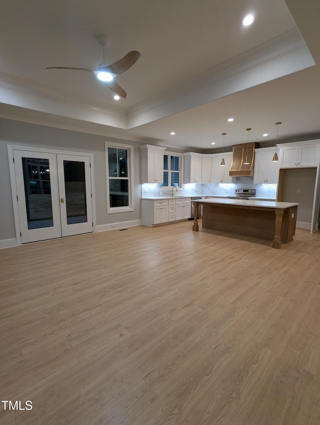 kitchen featuring a center island, white cabinetry, a tray ceiling, premium range hood, and decorative light fixtures