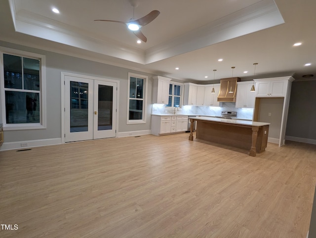 kitchen with decorative light fixtures, a kitchen island, a tray ceiling, custom range hood, and white cabinets