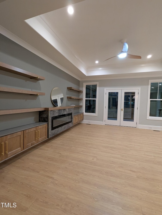 unfurnished living room featuring light hardwood / wood-style floors, ceiling fan, a fireplace, a raised ceiling, and ornamental molding