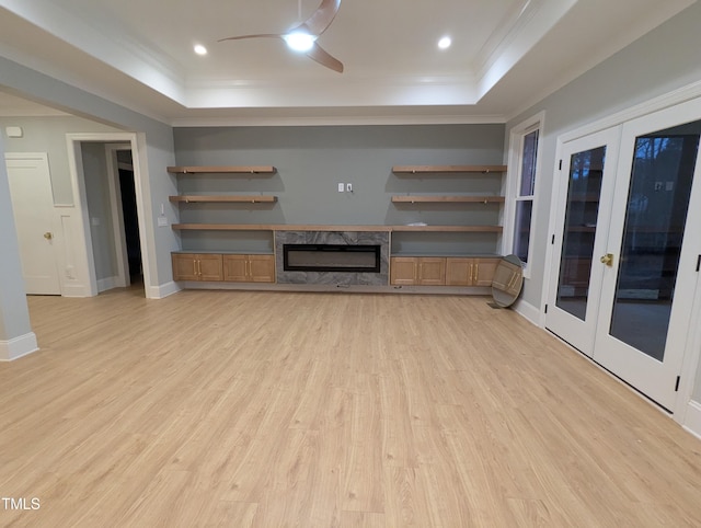 unfurnished living room with light wood-type flooring, a tray ceiling, and ornamental molding