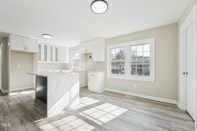 kitchen with light stone countertops, a center island, sink, white cabinets, and light wood-type flooring