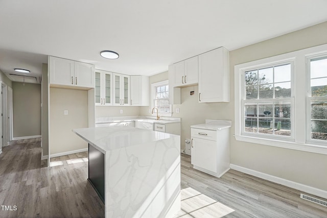 kitchen with a kitchen island, light wood-type flooring, white cabinetry, and light stone counters