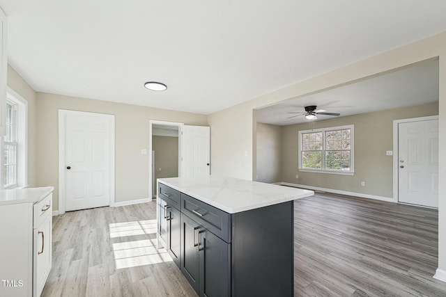 kitchen with ceiling fan, a kitchen island, light hardwood / wood-style floors, light stone counters, and white cabinetry