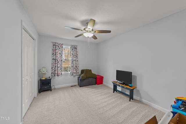 living area with light carpet, a textured ceiling, ceiling fan, and a wood stove