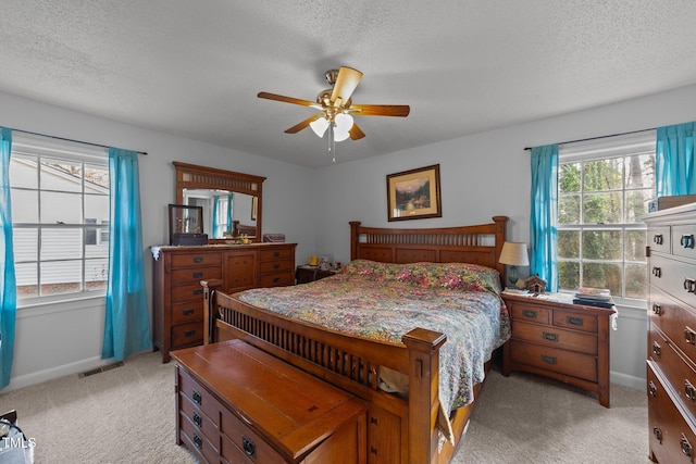 bedroom with ceiling fan, light colored carpet, and a textured ceiling