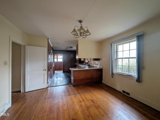 kitchen with kitchen peninsula, hanging light fixtures, a notable chandelier, and light hardwood / wood-style floors