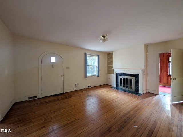 unfurnished living room featuring built in shelves, hardwood / wood-style floors, and a high end fireplace