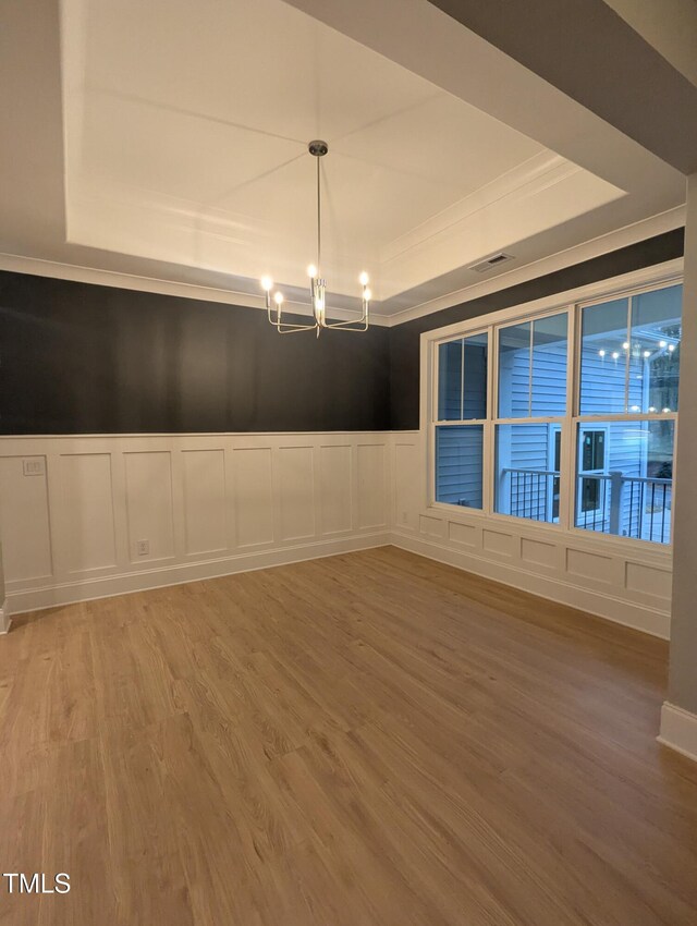 spare room with a notable chandelier, ornamental molding, a raised ceiling, and wood-type flooring