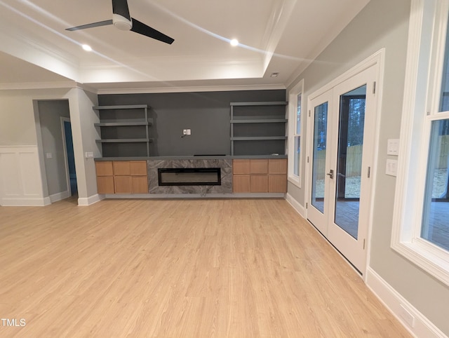 unfurnished living room featuring light hardwood / wood-style flooring, built in shelves, a high end fireplace, a raised ceiling, and french doors