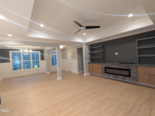 unfurnished living room with ornamental molding, ceiling fan, light wood-type flooring, and a high end fireplace