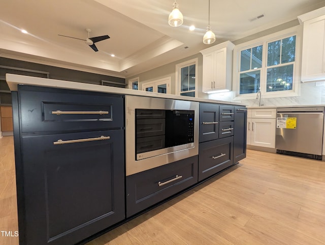 kitchen featuring hanging light fixtures, stainless steel appliances, a tray ceiling, light wood-type flooring, and white cabinetry