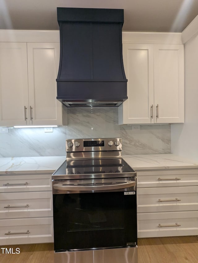 kitchen featuring custom exhaust hood, stainless steel range with electric stovetop, light hardwood / wood-style floors, white cabinets, and tasteful backsplash